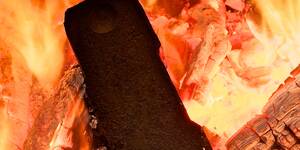 Du siehst ein brennendes Holzbrikett inmitten von Glut und Flammen in einem Kamin oder Ofen.