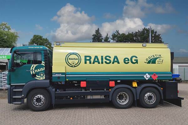 Du siehst einen RAISA eG Tankwagen in grün-gelber Farbe für Heizöl- oder Kraftstofflogistik auf einem Hof.