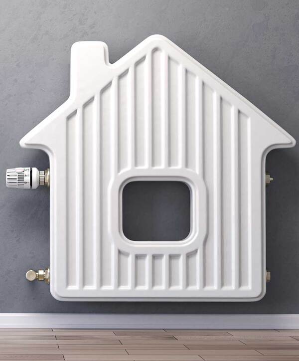 Du siehst einen weißen Heizkörper in Hausform an einer grauen Wand mit Holzfußboden davor.